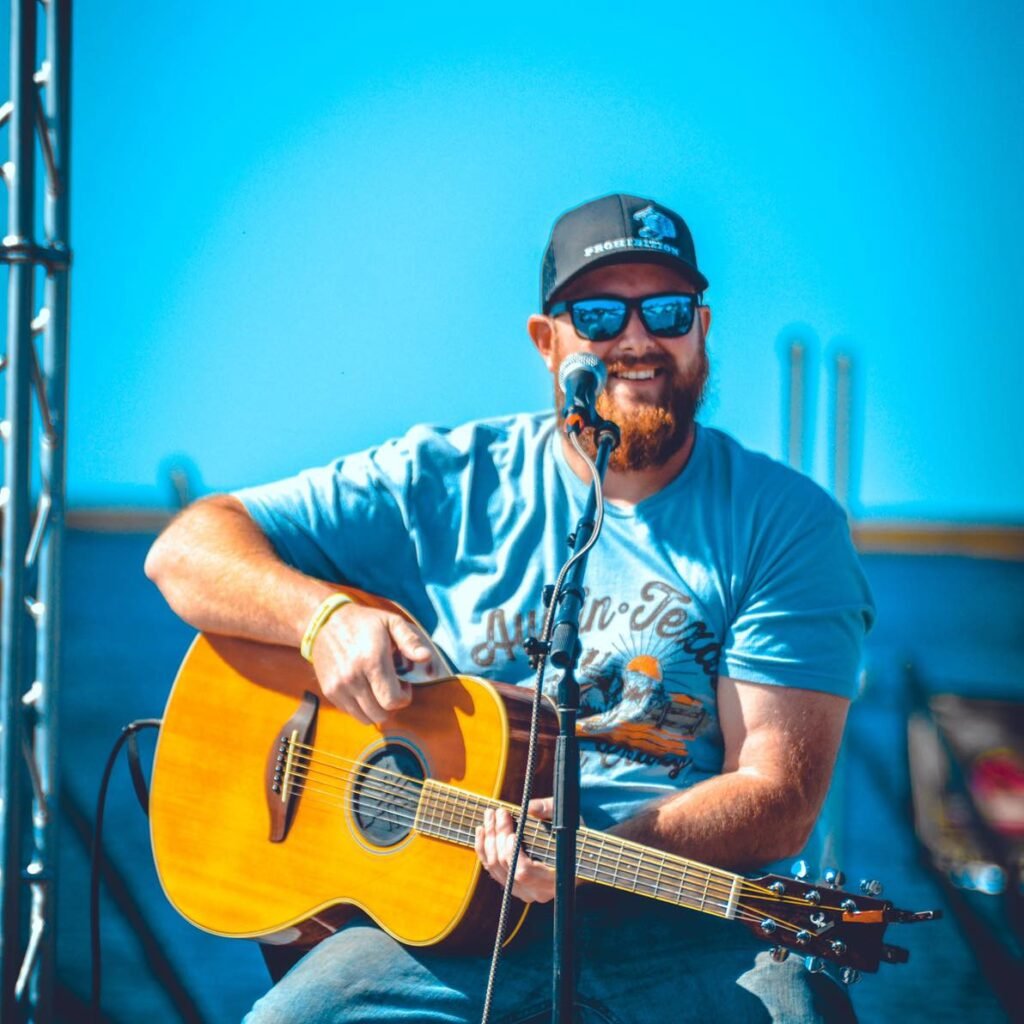 Josh Nettles performing live on stage in North Florida, singing and playing guitar under warm concert lighting.