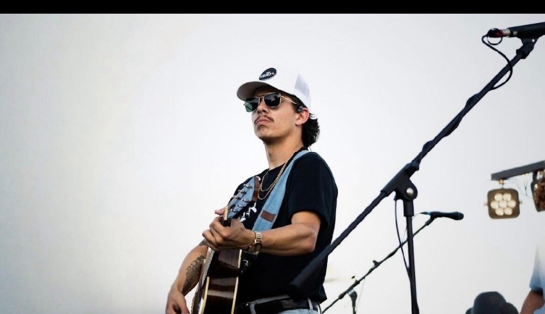 Cam Wheaton performing live on stage in North Florida with an acoustic guitar.